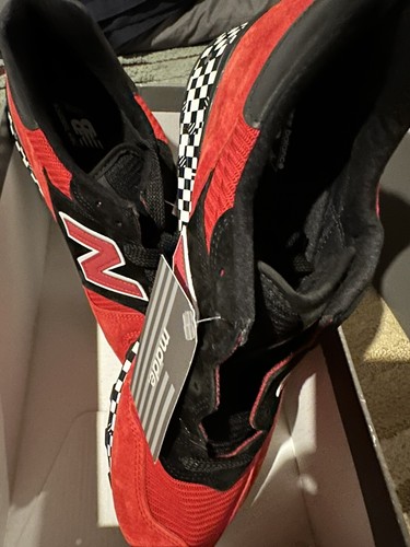 Red and black New Balance 1300AP sneakers with white checkered flag design, suede panels, and gray Made In USA tag.