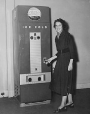 Woman demonstrates one of new soft drink slot machines which will - Old Photo