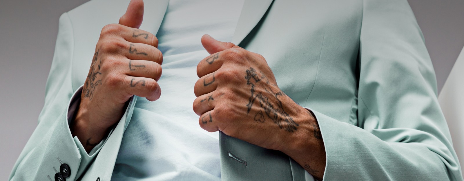 Eine Person mit Tattoos trägt eine helle Anzugsjacke über einem weißen Shirt.