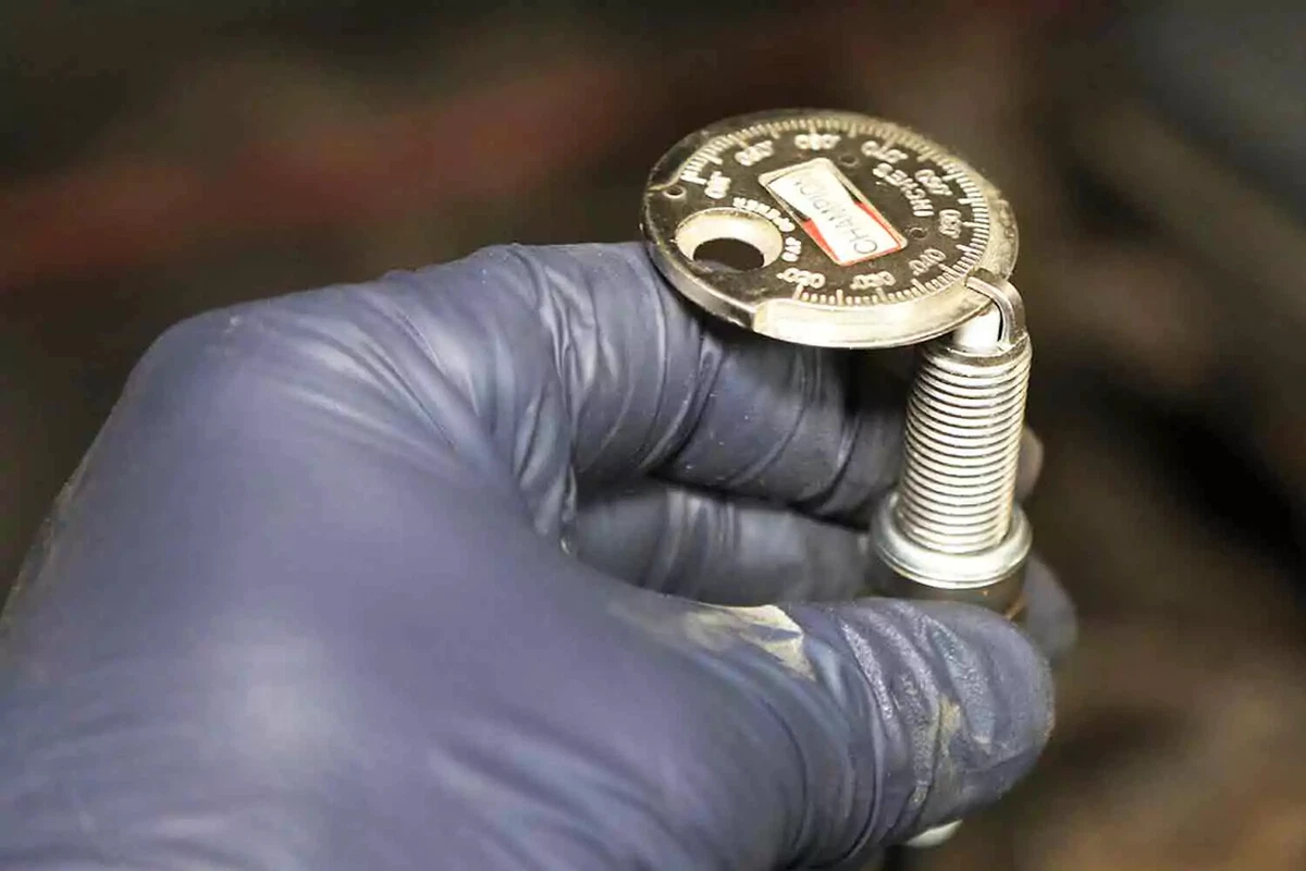 A mechanic wearing a blue nitrile glove checking the gap on a spark plug.
