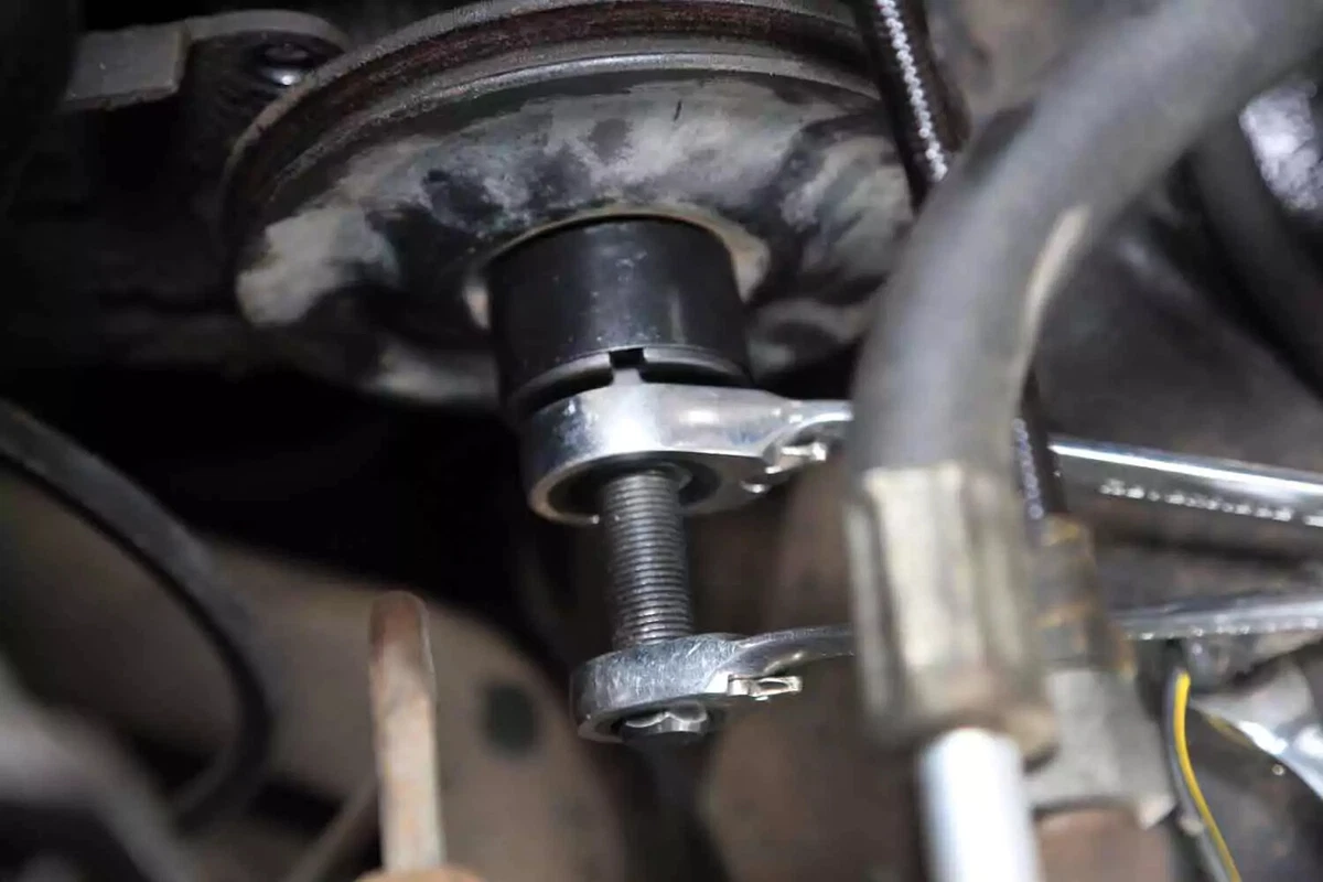 A mechanic uses two box wrenches and a clamshell puller tool to remove the power steering pump pulley.
