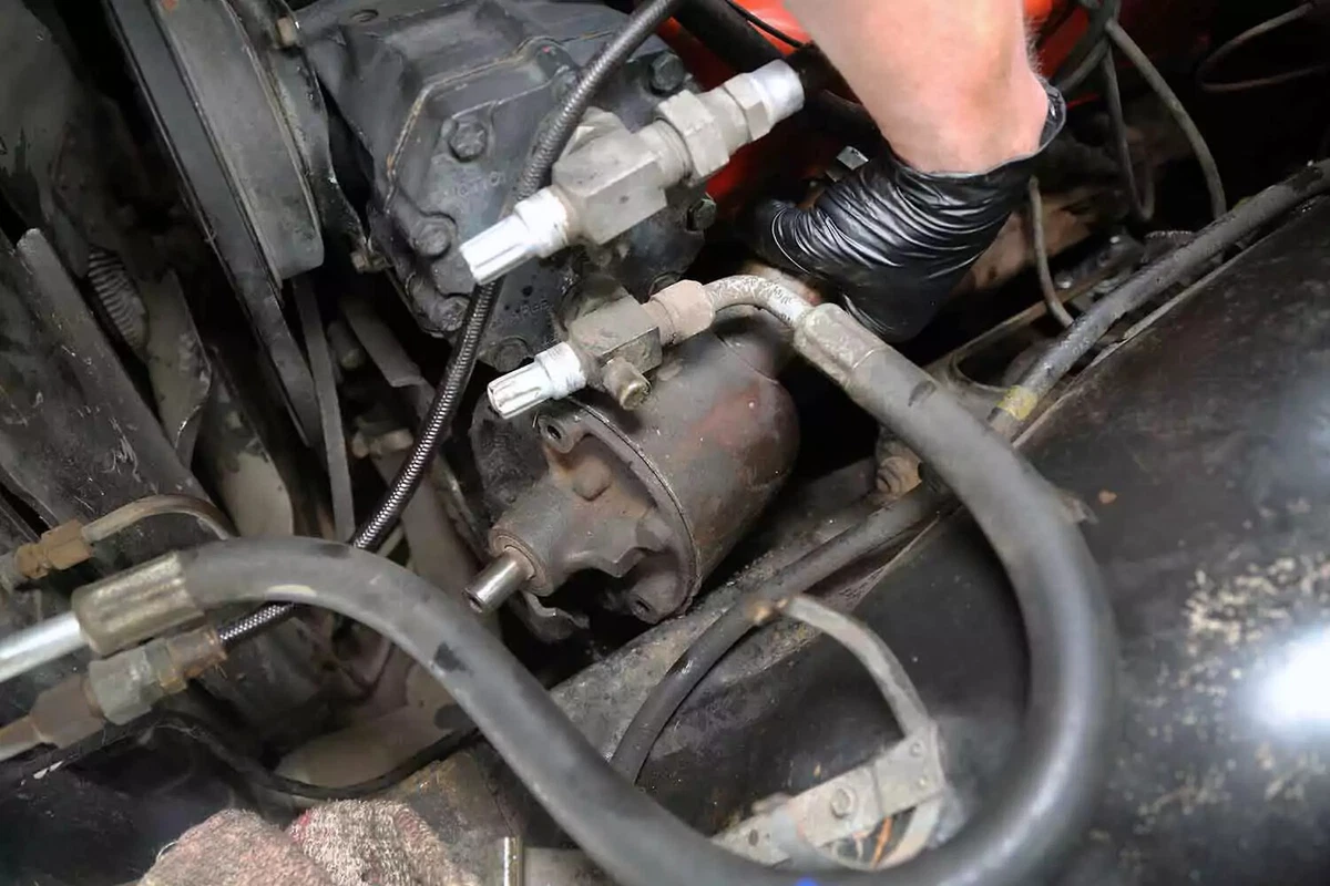 A mechanic maneuvers the steering pump away from the engine.