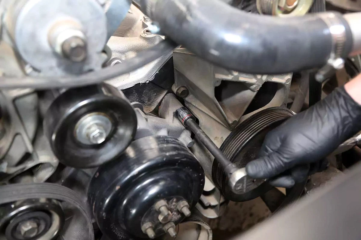A ratchet wrench is used to remove a water pump bolt.