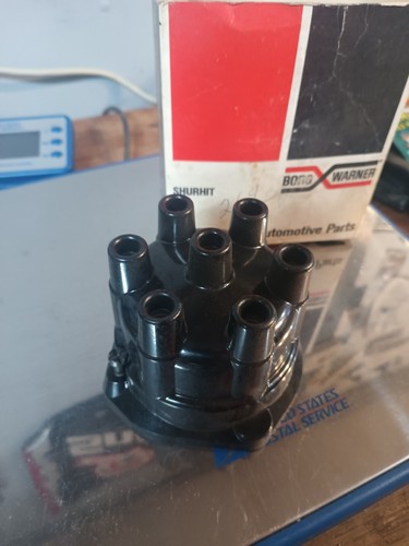 Black Borg-Warner 6-cyl conventional distributor cap with eight spark plugs, made in USA, shown in front of a red box.