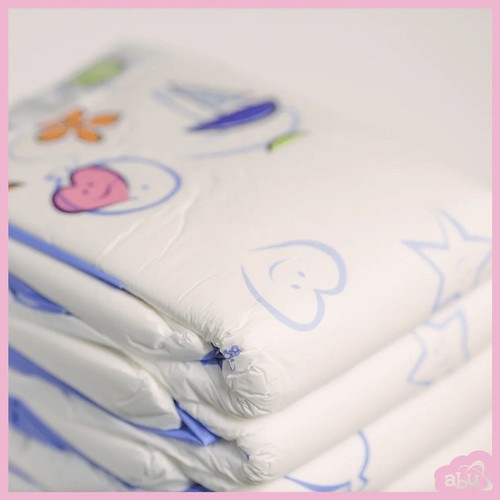 White ABU Cushies plastic back with pastel bear, bird, and heart graphic on blue background, folded on pink surface.