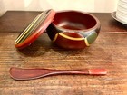 Brown lacquerware bowl with gold-edged rim, lid, and side handle, featuring colorful geometric patterns.