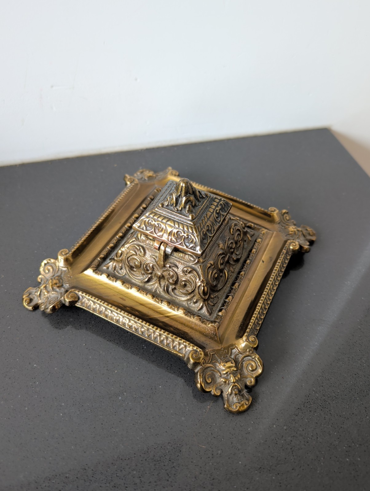 An ornate cast brass inkwell with a decorative figural lid.