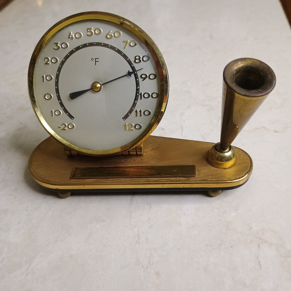 A gold-tone MCM desk thermometer and pen holder combo — the kind of retro office gadget that actually tells the room's temperature while looking impossibly suave.