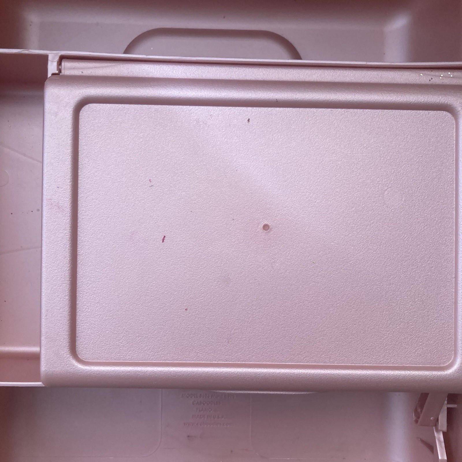 Pink rectangular Caboodle makeup case with textured lid, featuring small circular hole near top center.