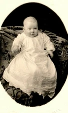 smiling Infant girl in beautiful outfit sitting in large chai 1910s era RPPC TT1