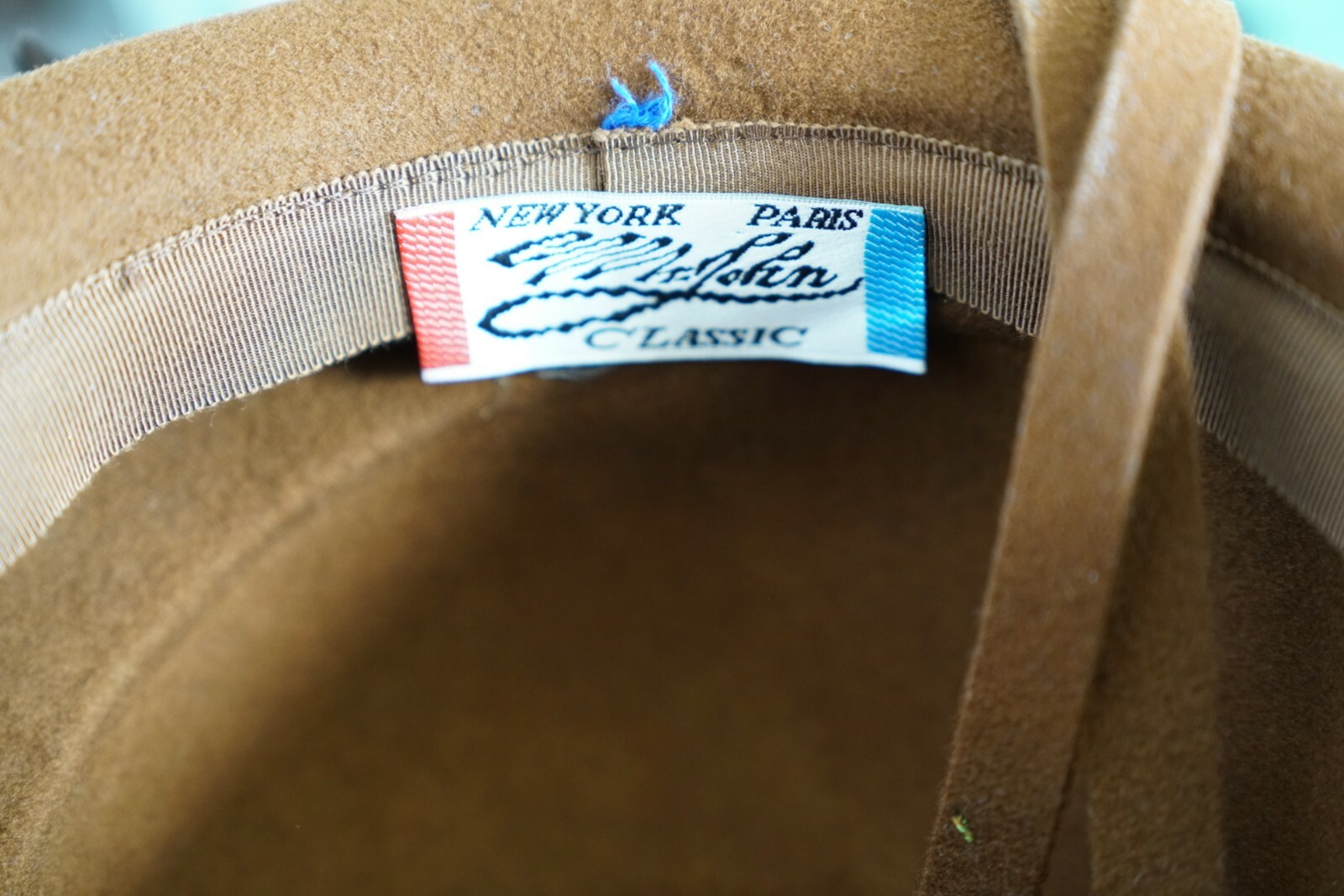 Brown hat with blue and red New York Paris label reading “Feather Classic” and “100% Wool” inside the cream lining.