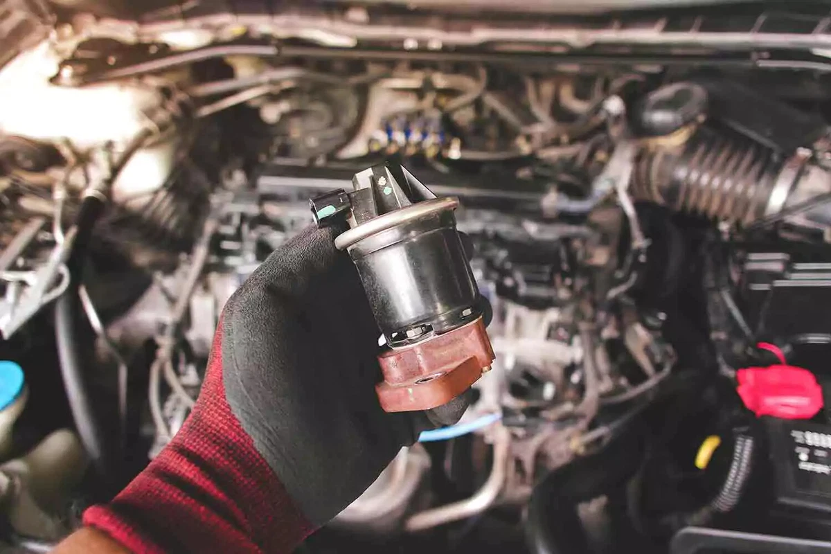 A mechanic holds an EGR valve removed from the vehicle's engine during a DIY replacement.