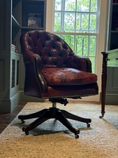 A CAPTAINS DESK CHAIR. upholstered in red leather, with a deep buttoned back.