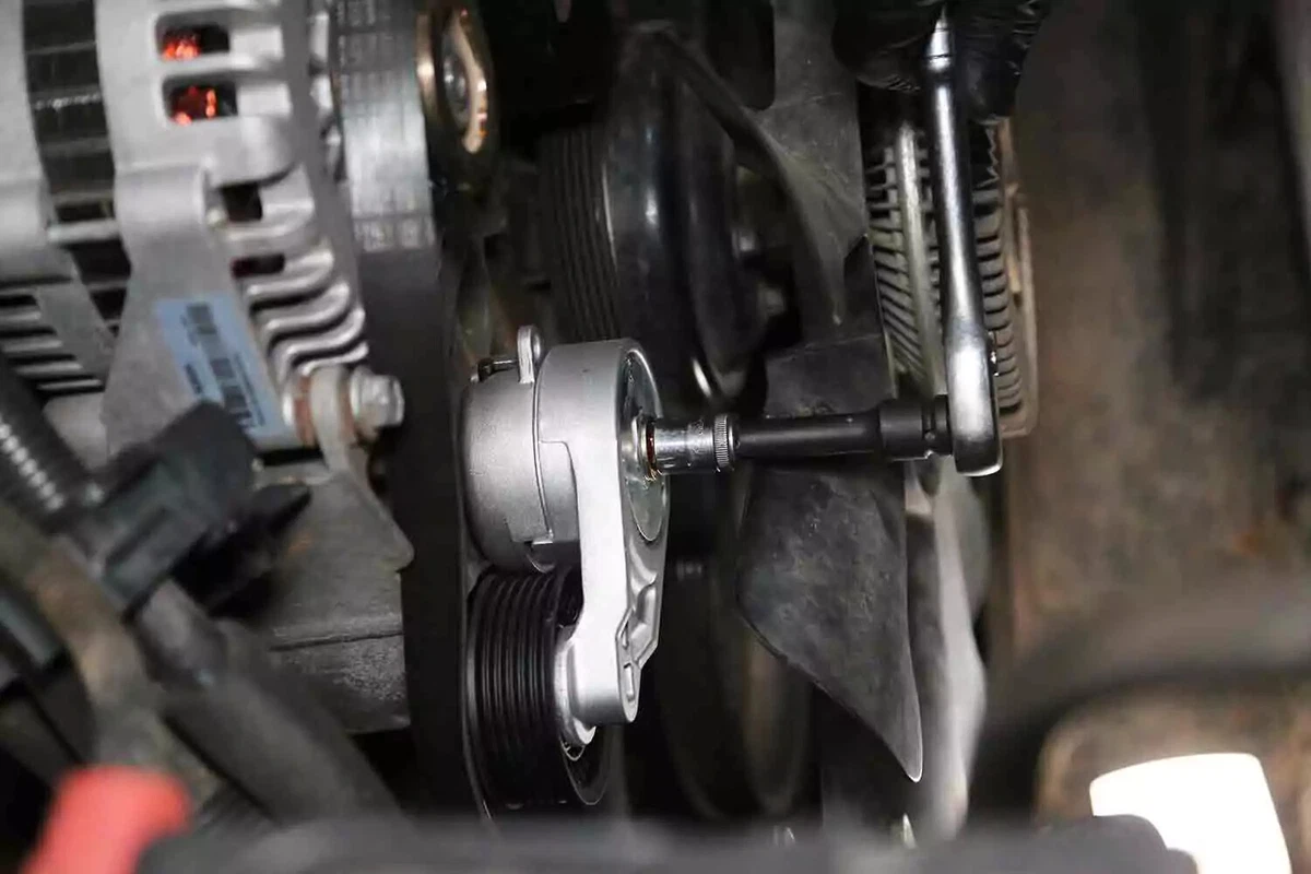 A socket wrench in the process of unbolting the tensioner.