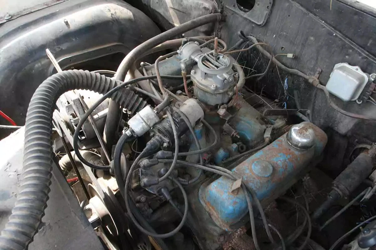 A weathered V-8 engine in an older vehicle, with a single ignition coil.