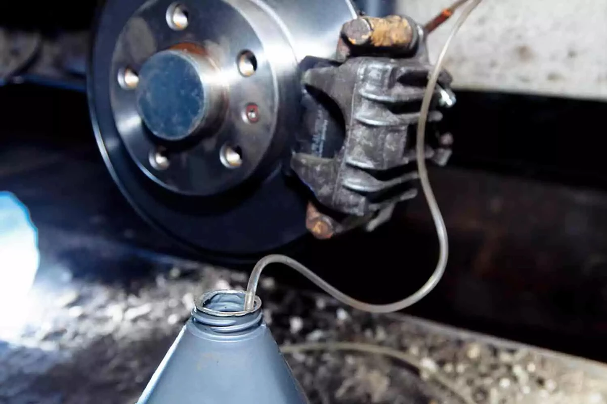Bleeding brake fluid from a disc brake system using a clear plastic hose and a gray drain jug.