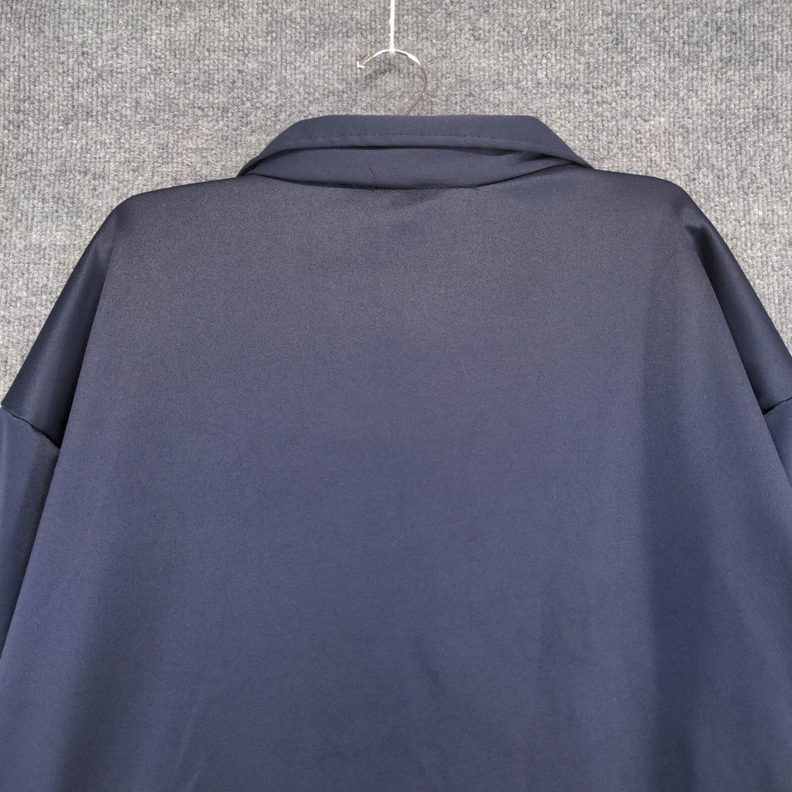Dark blue men's full zip jacket with notch lapel, hanging on white hanger against light gray textured background.