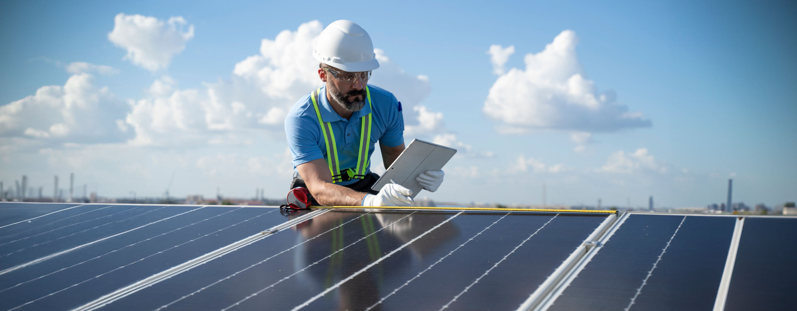 Ein Monteur installiert ein Solarpanel auf dem Dach, in der linken Hand hält er ein Tablet, in der rechten einen Kugelschreiber.