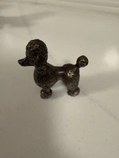 A stylized metal figurine of a coiﬀed poodle.