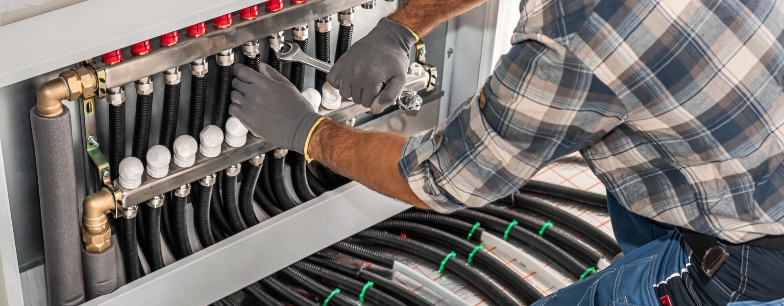Techniker bei der Arbeit an einem Heizkreisverteiler, der die Einstellungen und Anschlüsse eines Fußbodenheizungssystems überprüft