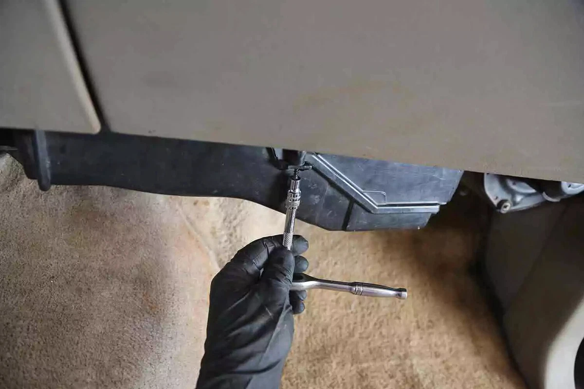 A mechanic wearing a black glove uses a ratchet to remove screws from the HVAC cover.