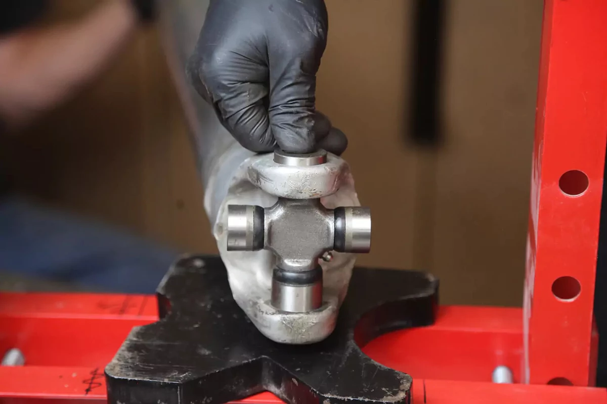 A mechanic wearing a black glove pushes a cap into a U-joint.
