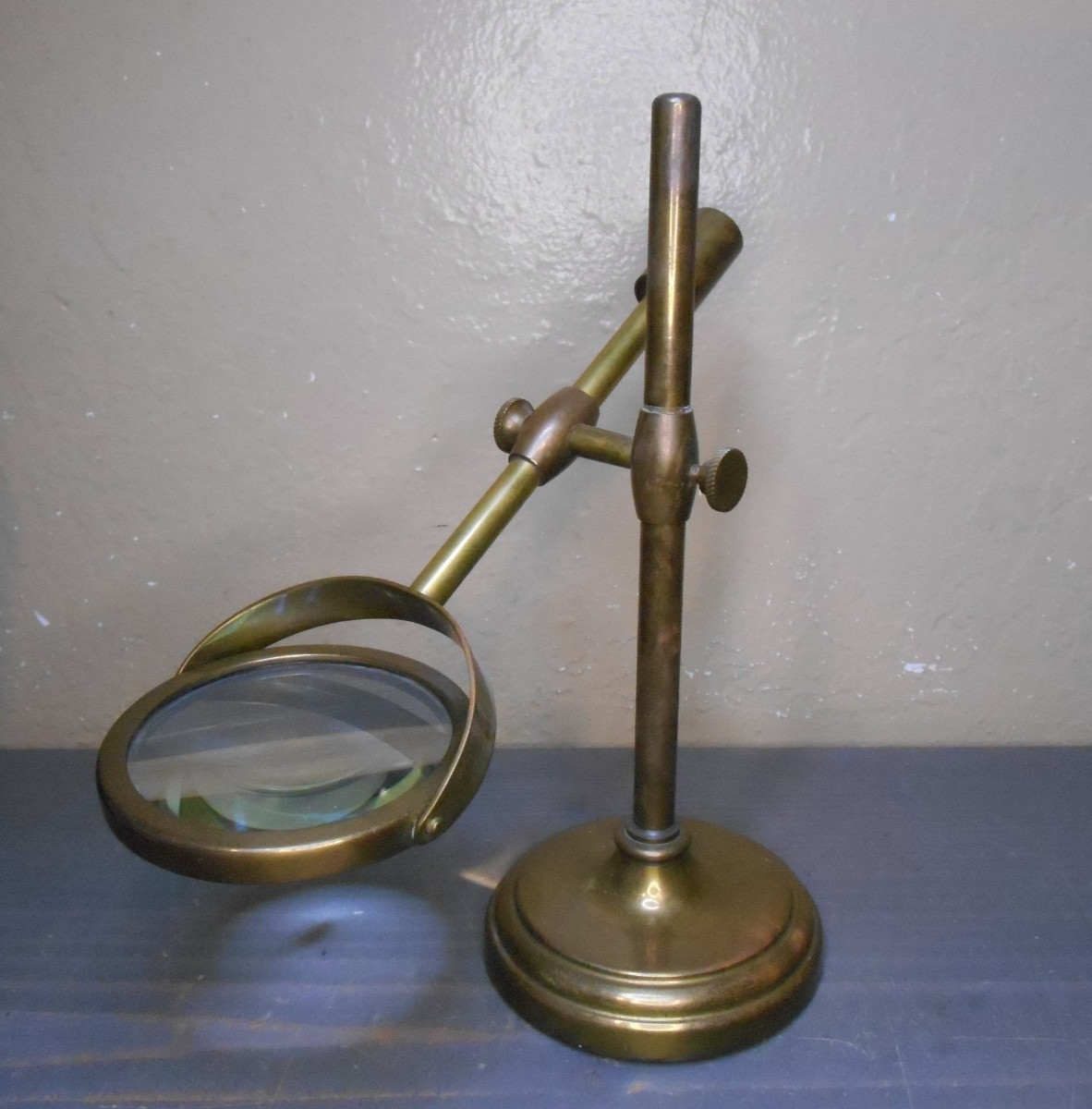 A brass magnifying glass mounted on an adjustable swing-arm stand.