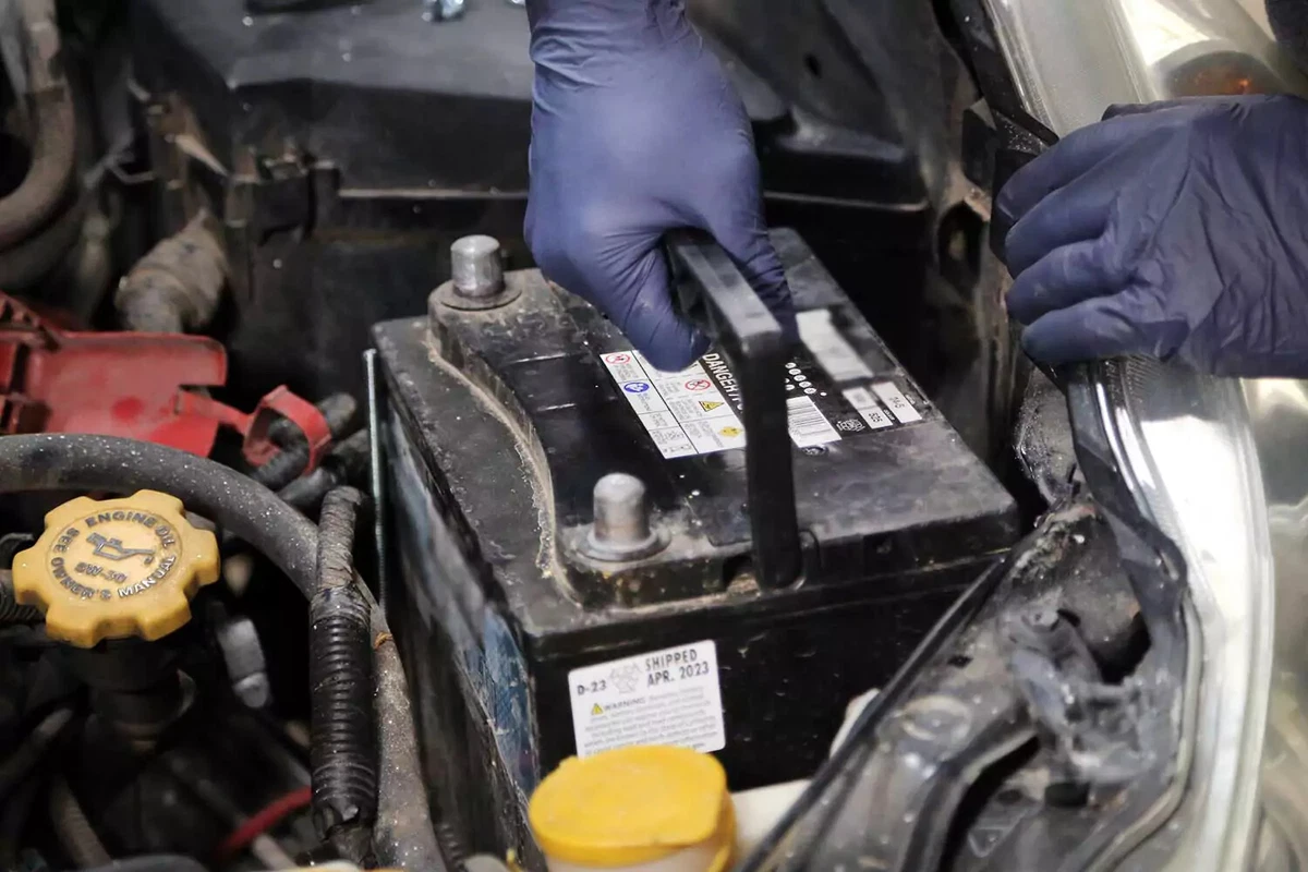 Removing a battery from a vehicle’s engine bay.
