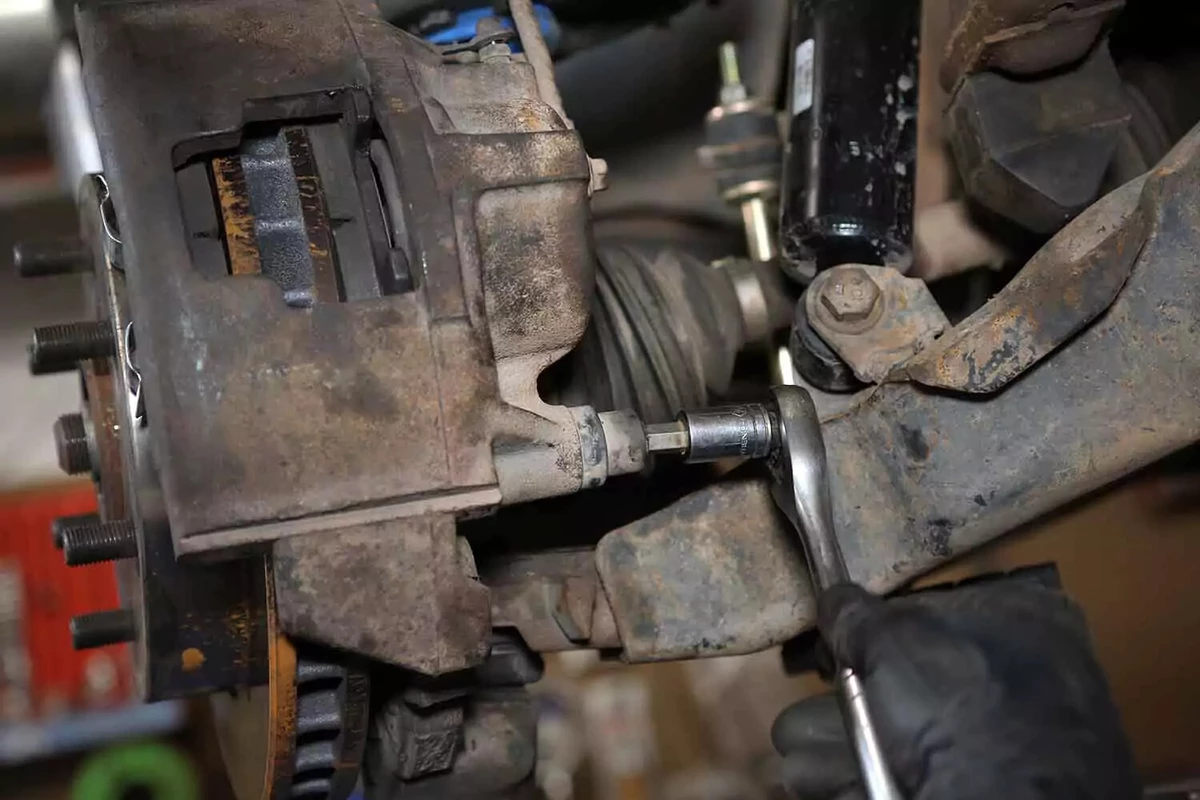 A mechanic unbolts a brake caliper with a socket wrench.
