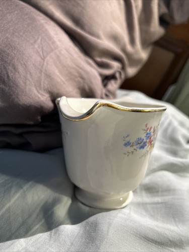 White ceramic cup with gold rim, floral print in blue and yellow, made in USA, lying on a light gray fabric surface.