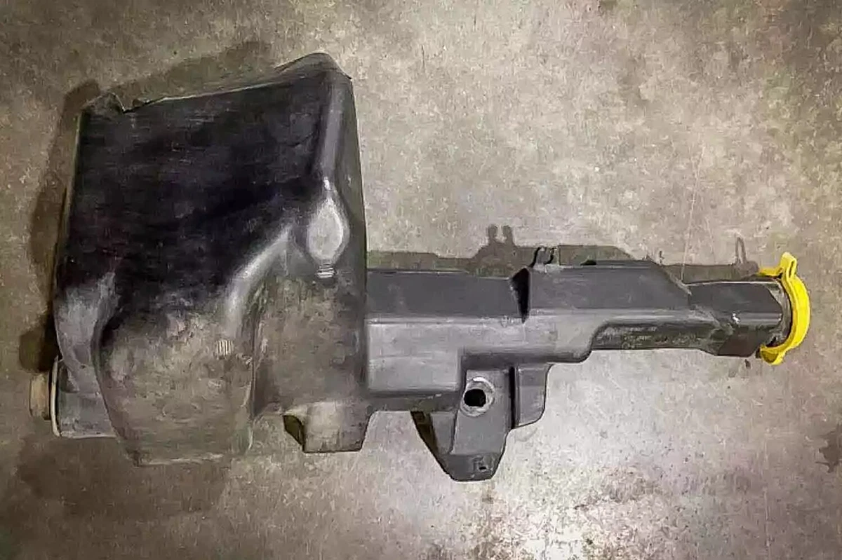 An OEM Dodge Ram 2500 windshield washer fluid reservoir with a yellow cap, displayed on a concrete surface.