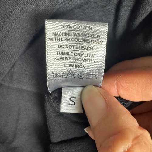 White NWOT label on black crewneck short sleeve shirt with size S, washing instructions, and red fabric composition.