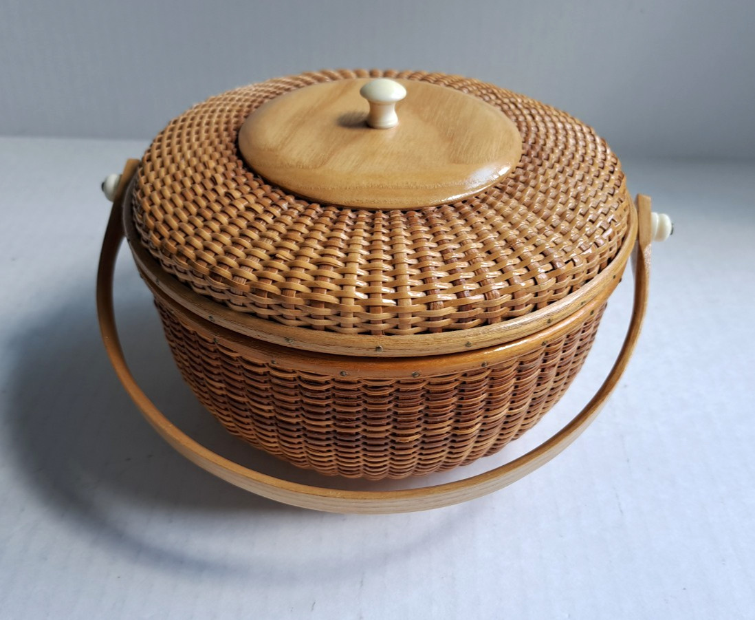 Round lidded Nantucket-style basket with a turned wood knob and swing handle, shown on a white background.