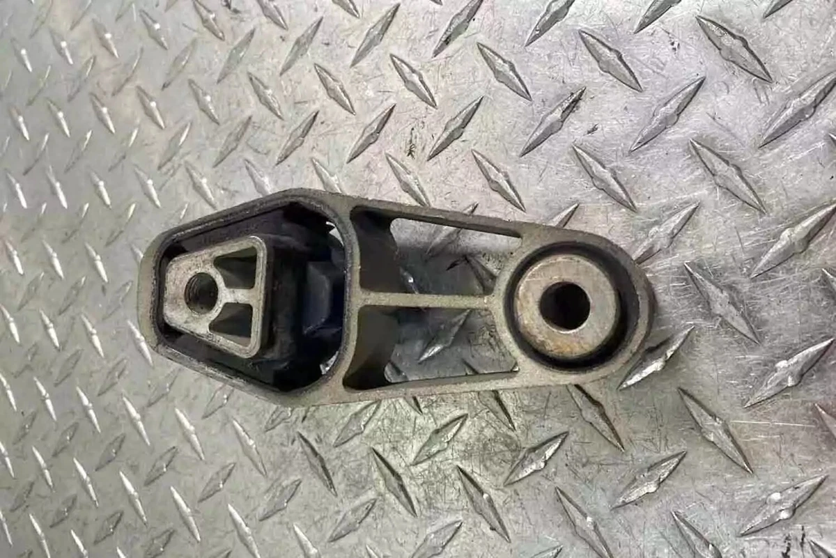 A previously-owned 2007-2015 MINI Cooper R55-R59 transmission mount displayed on a metal diamond-plate surface.
