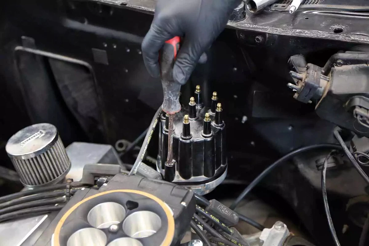 A mechanic removes the distributor cap with a nut driver.
