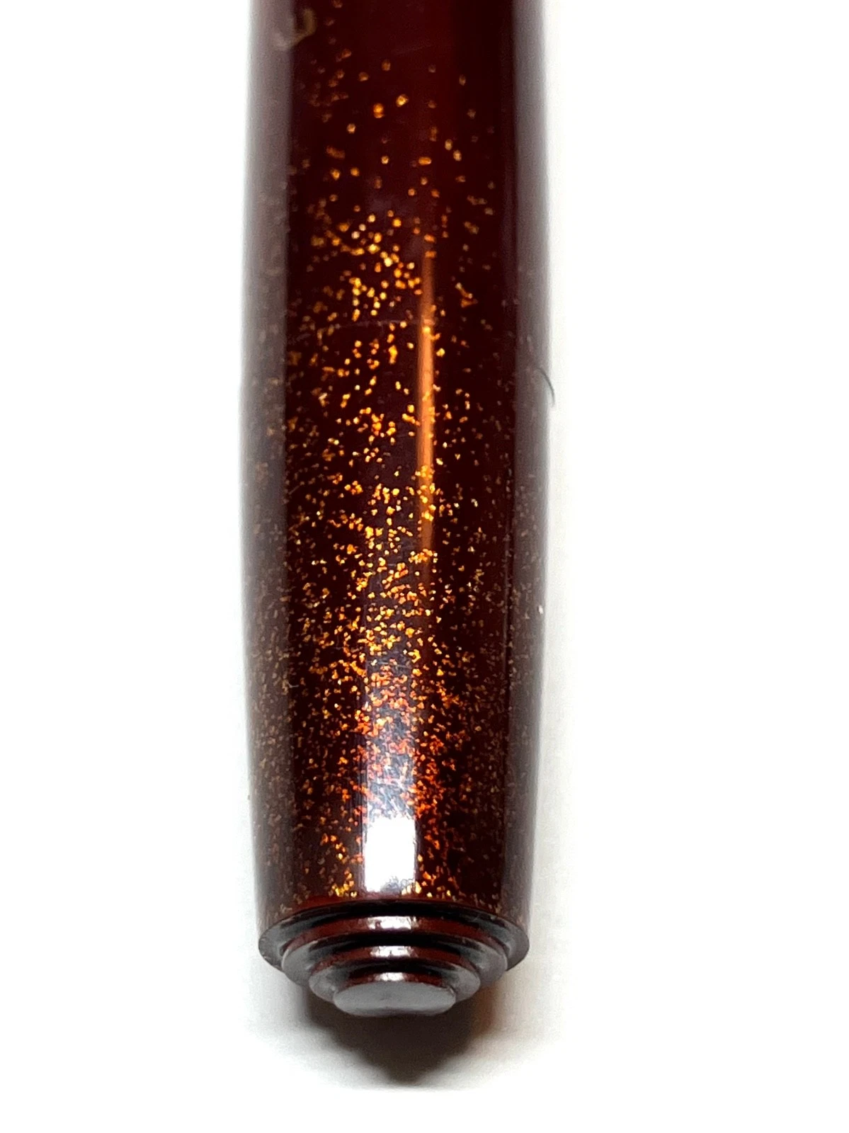 Close-up of brown vintage ink pen with gold glitter particles on barrel, resting on white background.
