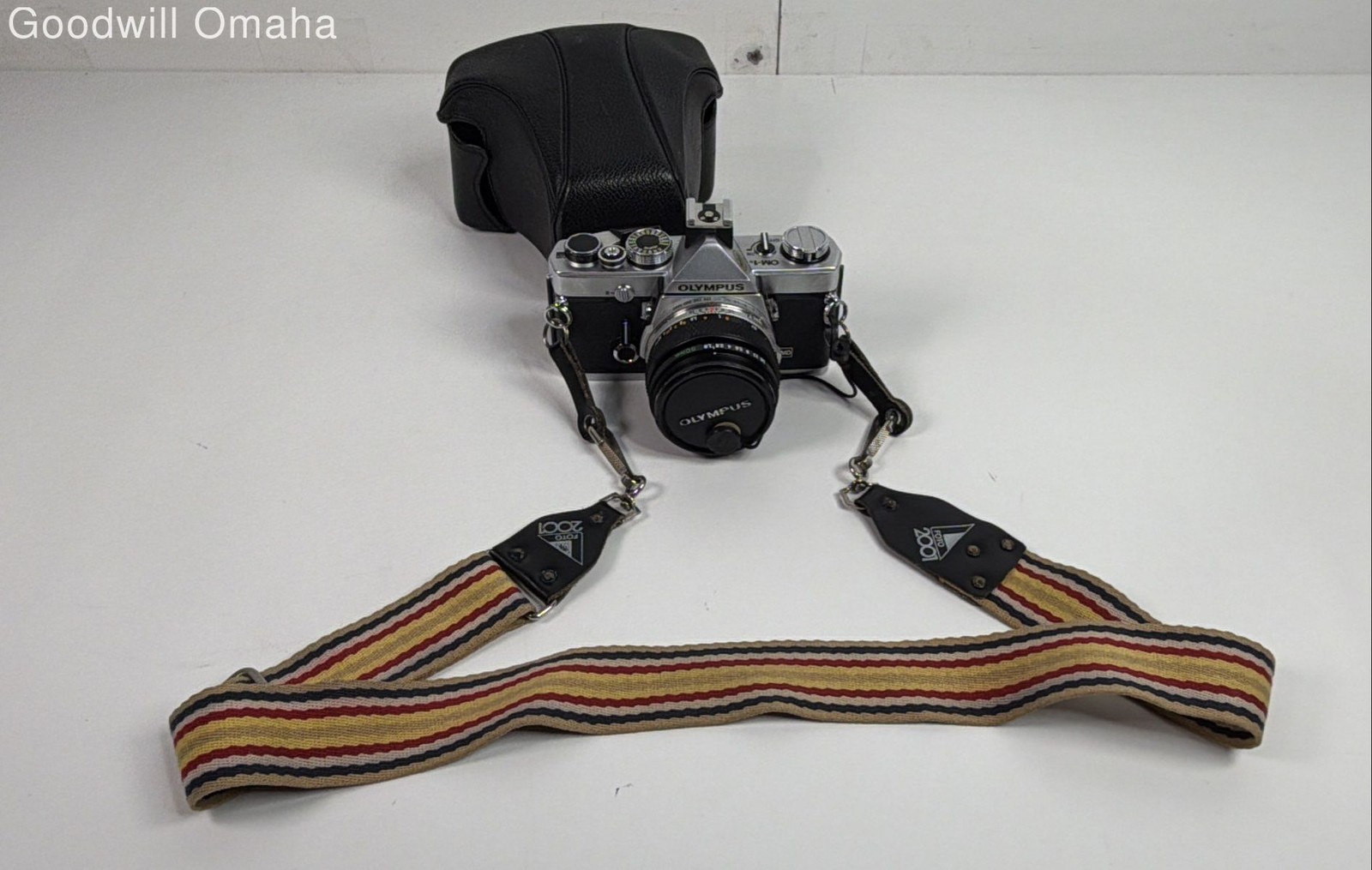 Silver and black Olympus OM-1 35mm SLR film camera shown with its fitted leather case