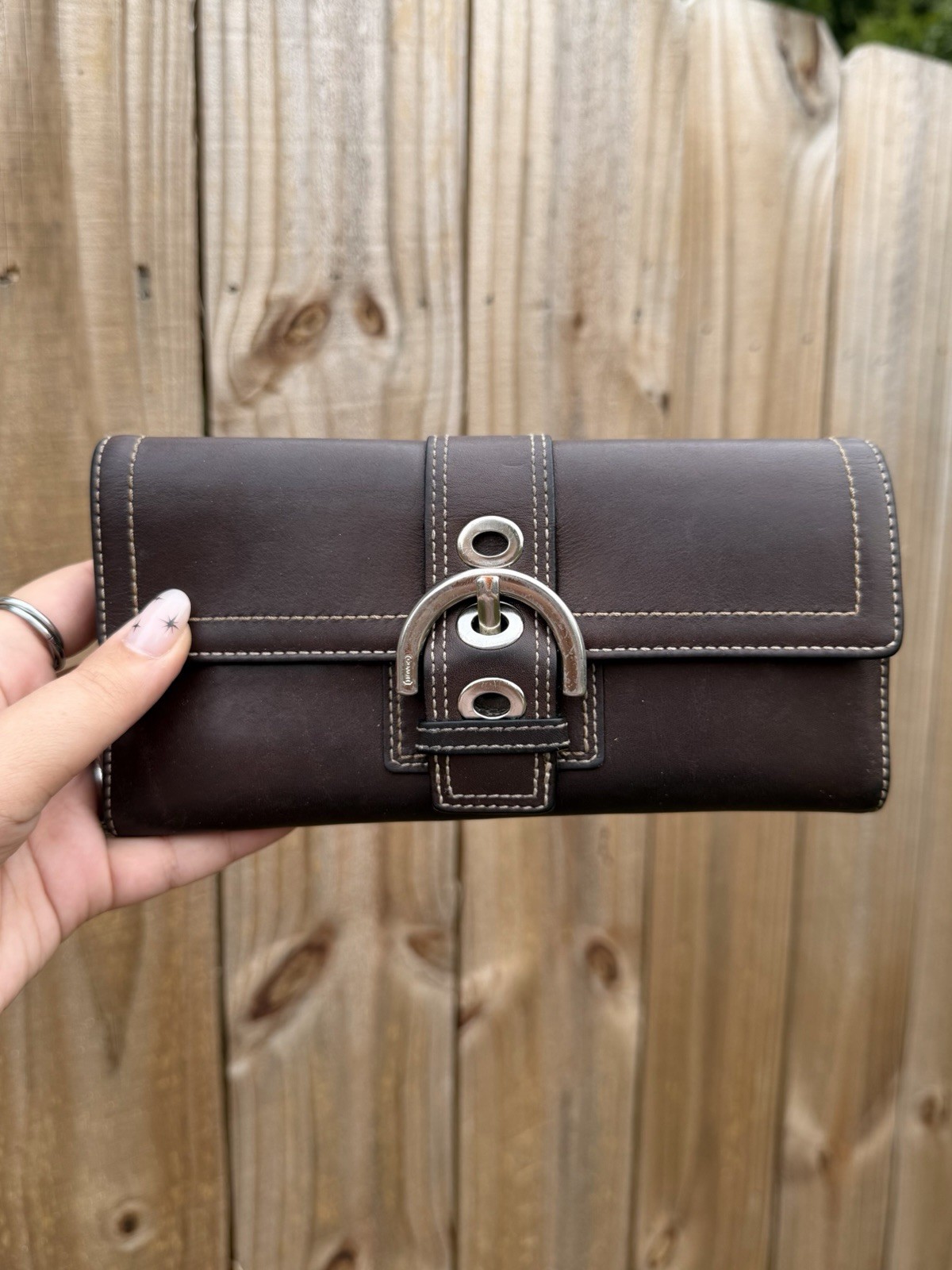 A brown smooth leather envelope-style wallet with a small buckle closure, shown closed.