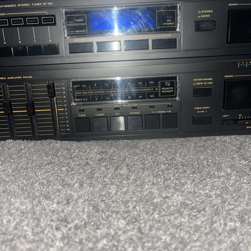 Black Marantz ST-100 tuner and PM100 amplifier with gold lettering, sliders, buttons, and digital displays on carpet.