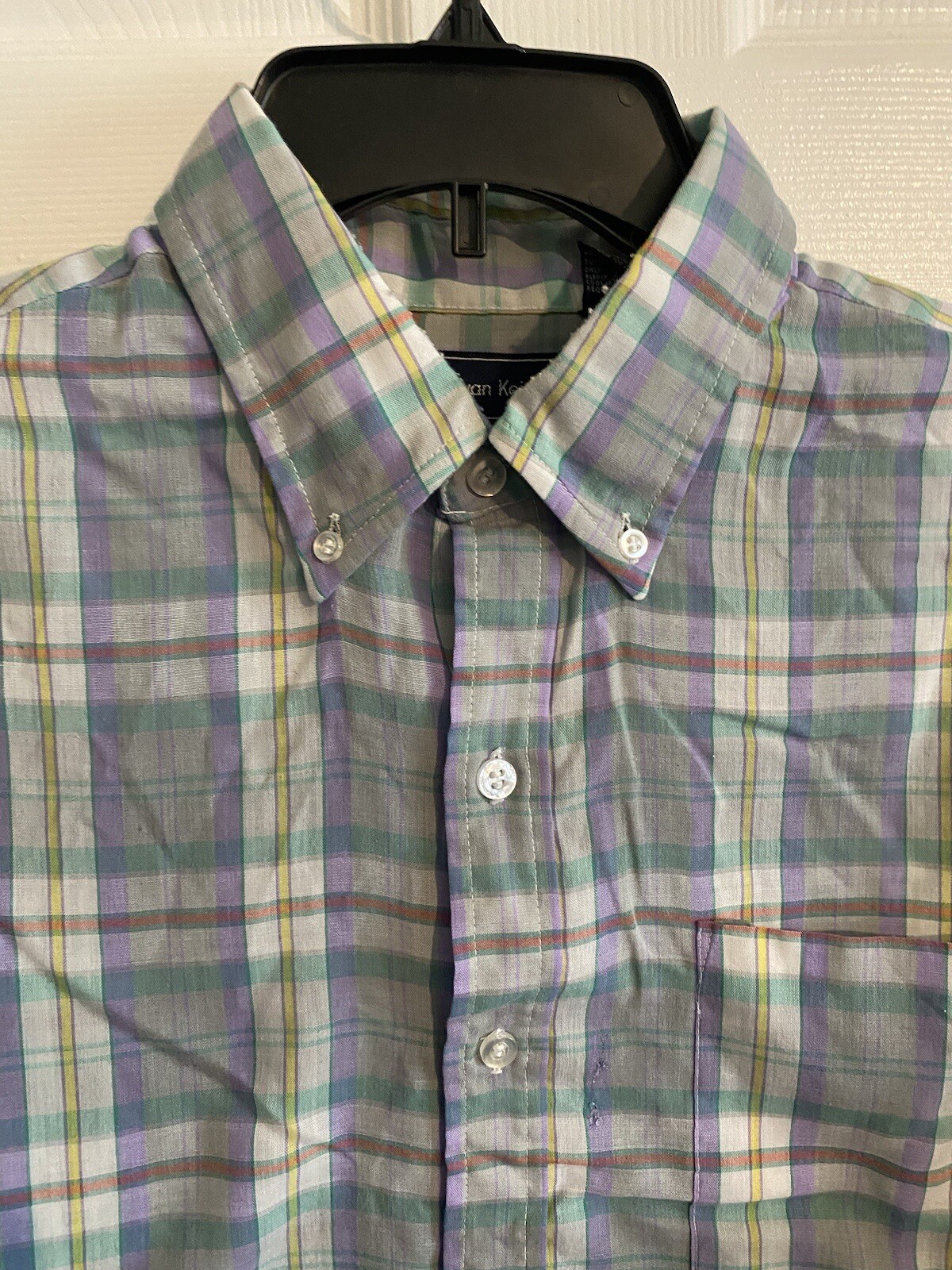 Men’s long-sleeve button-up shirt with purple, green, and yellow plaid pattern and chest pocket, hanging on black hanger.