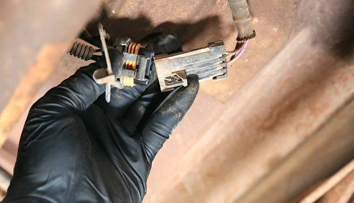 A mechanic wearing a black nitrile glove checks the O2 sensor wiring.