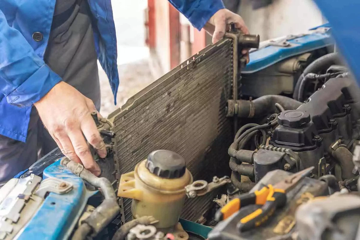 A mechanic removes an old damaged radiator from the front of the engine bay.