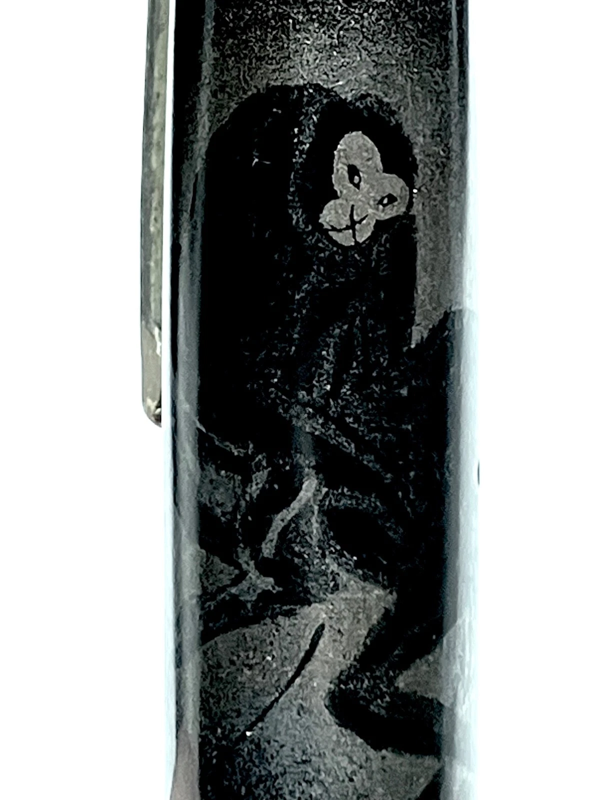 Black ink shut off fountain pen with white monkey design on barrel, resting on light sand with visible brushstrokes.