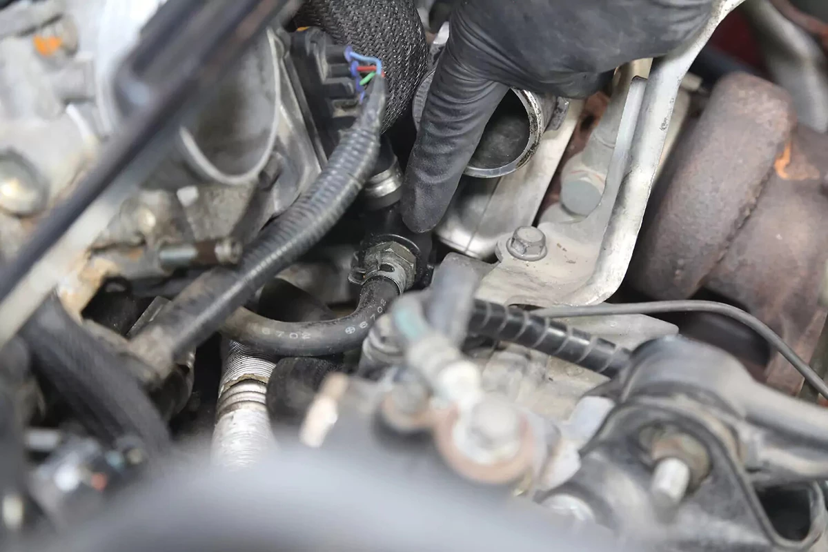 A mechanic wearing a black glove points to a vehicle's PCV valve.