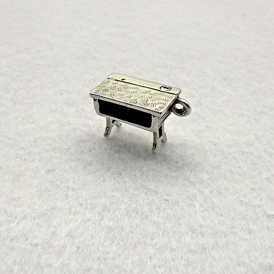 A tiny sterling silver school desk rendered as a dangle charm — a micro piece of nostalgia that actually belongs on a desk lover's bracelet or keychain.