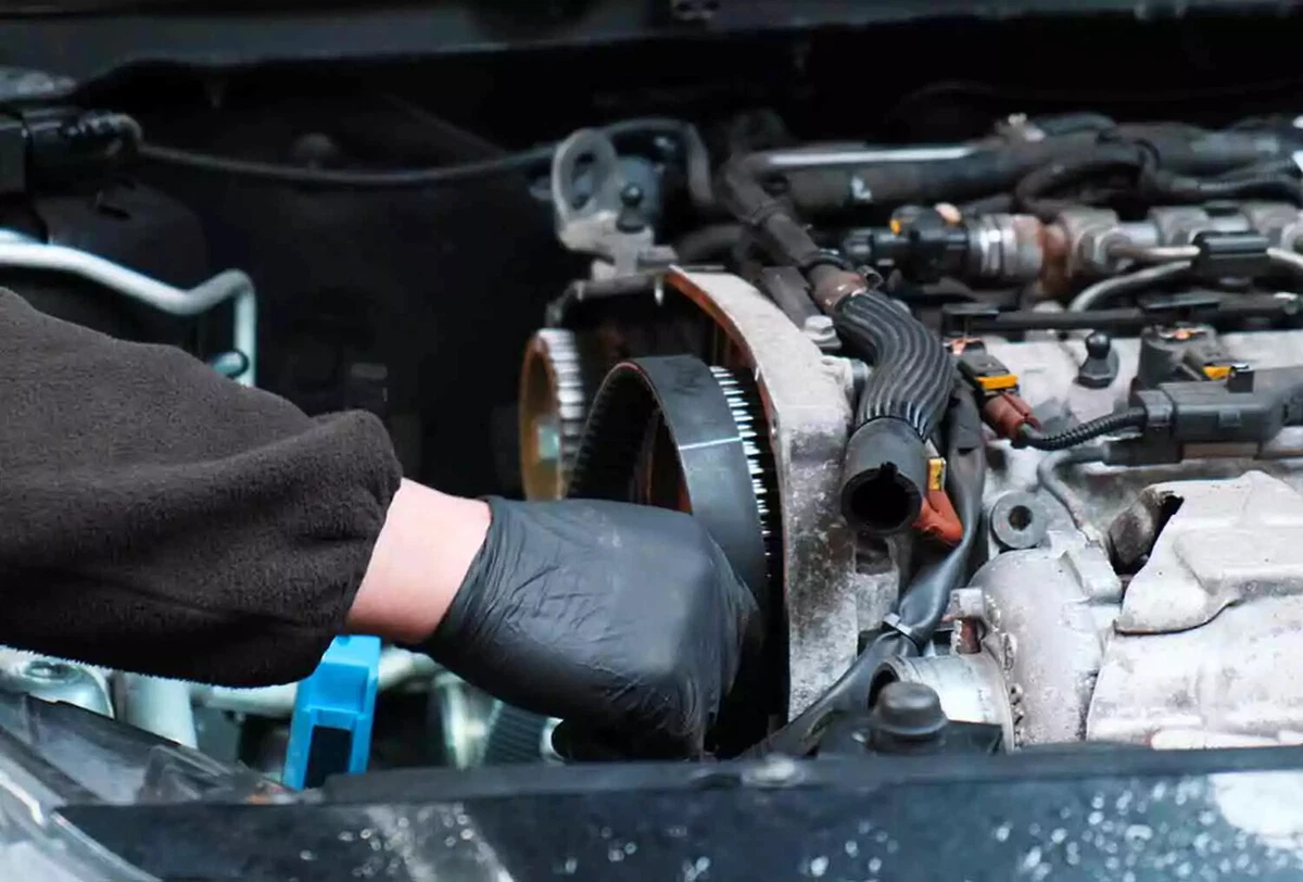 A mechanic wearing black nitrile gloves replaces a drive belt.