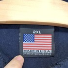 White fabric tag on blue “Made in U.S.A.” label, 2XL size, with American flag design and red, white, and gray text.