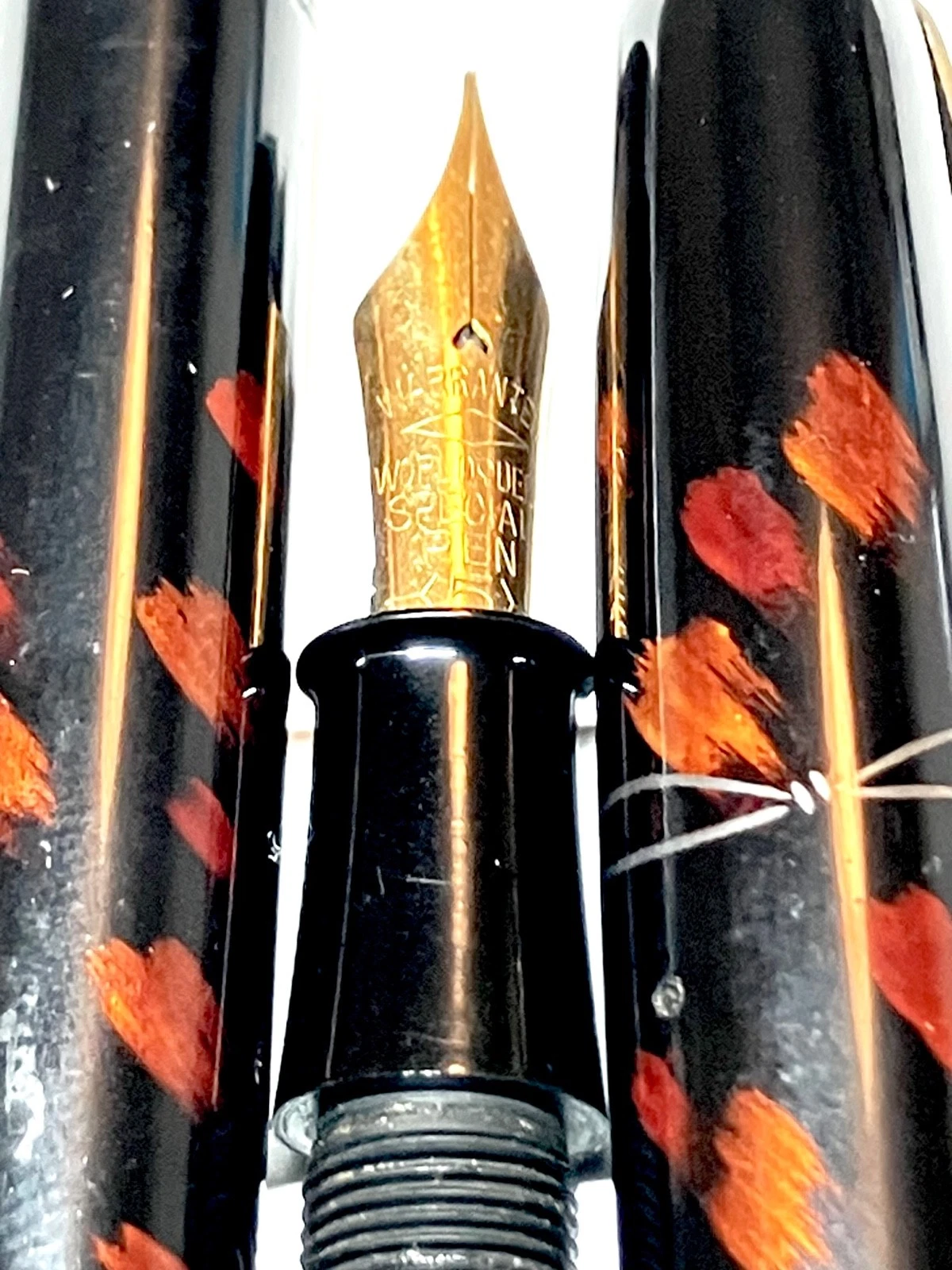 Vintage ink shut off fountain pen with gold nib, black body, and orange-red brushstroke pattern on barrel.