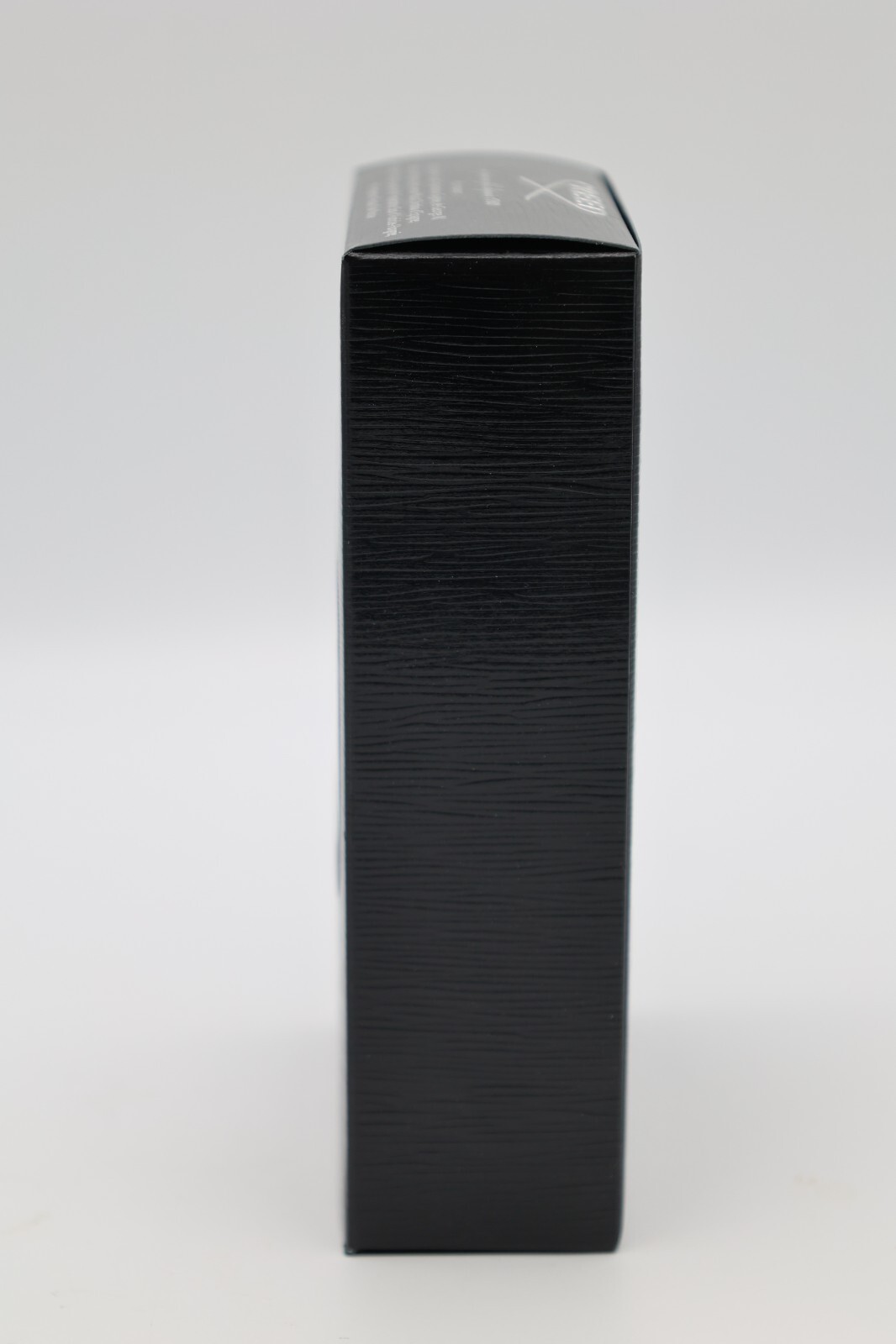 Black rectangular box with subtle horizontal grooves, white text and logo on top edge, standing upright.