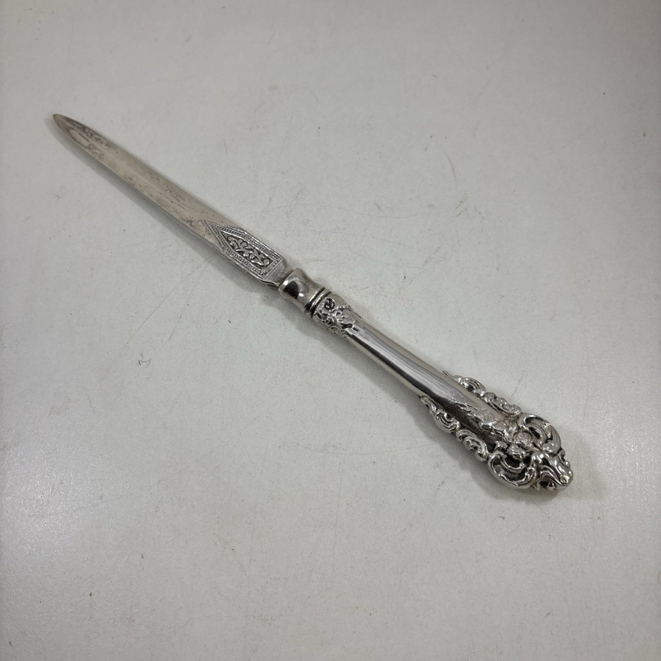An ornate silver plate letter opener with a decorative handle — the kind of desk piece that makes people ask "where did you get that?"